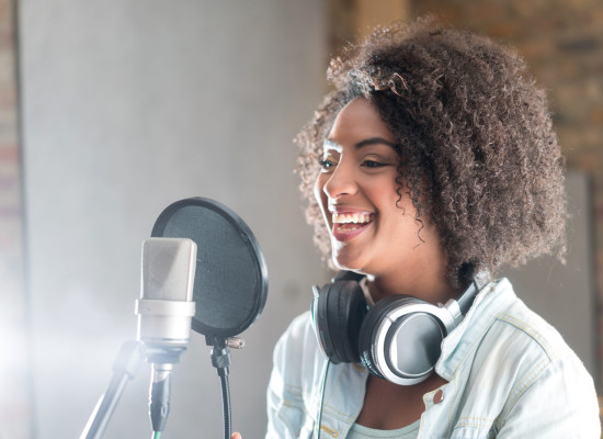 Beautiful young woman smiling behind the microphone at a recording studio and looking very happy